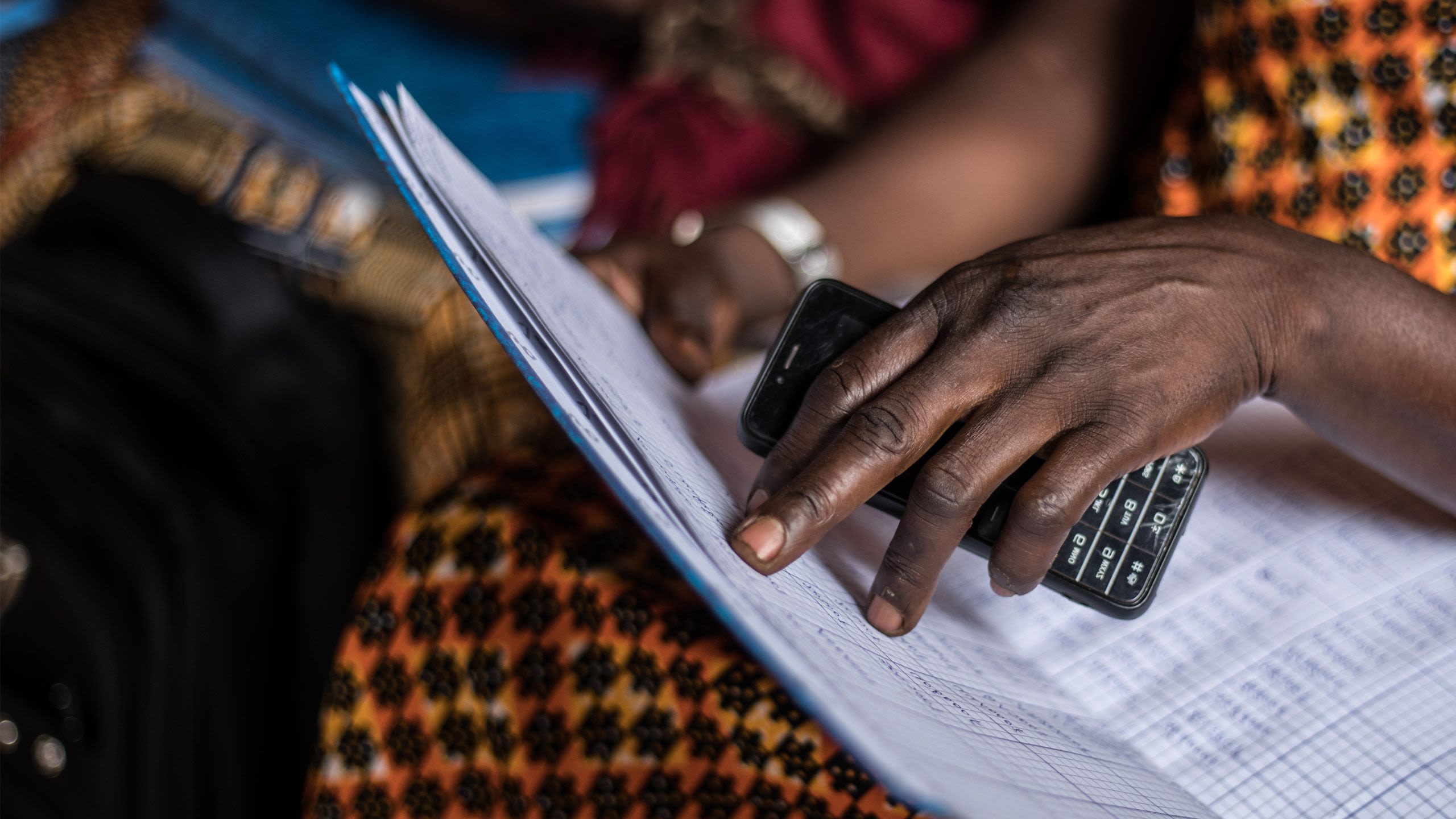 A close-up of a woman's hands holding a cell phone and a ledger.
