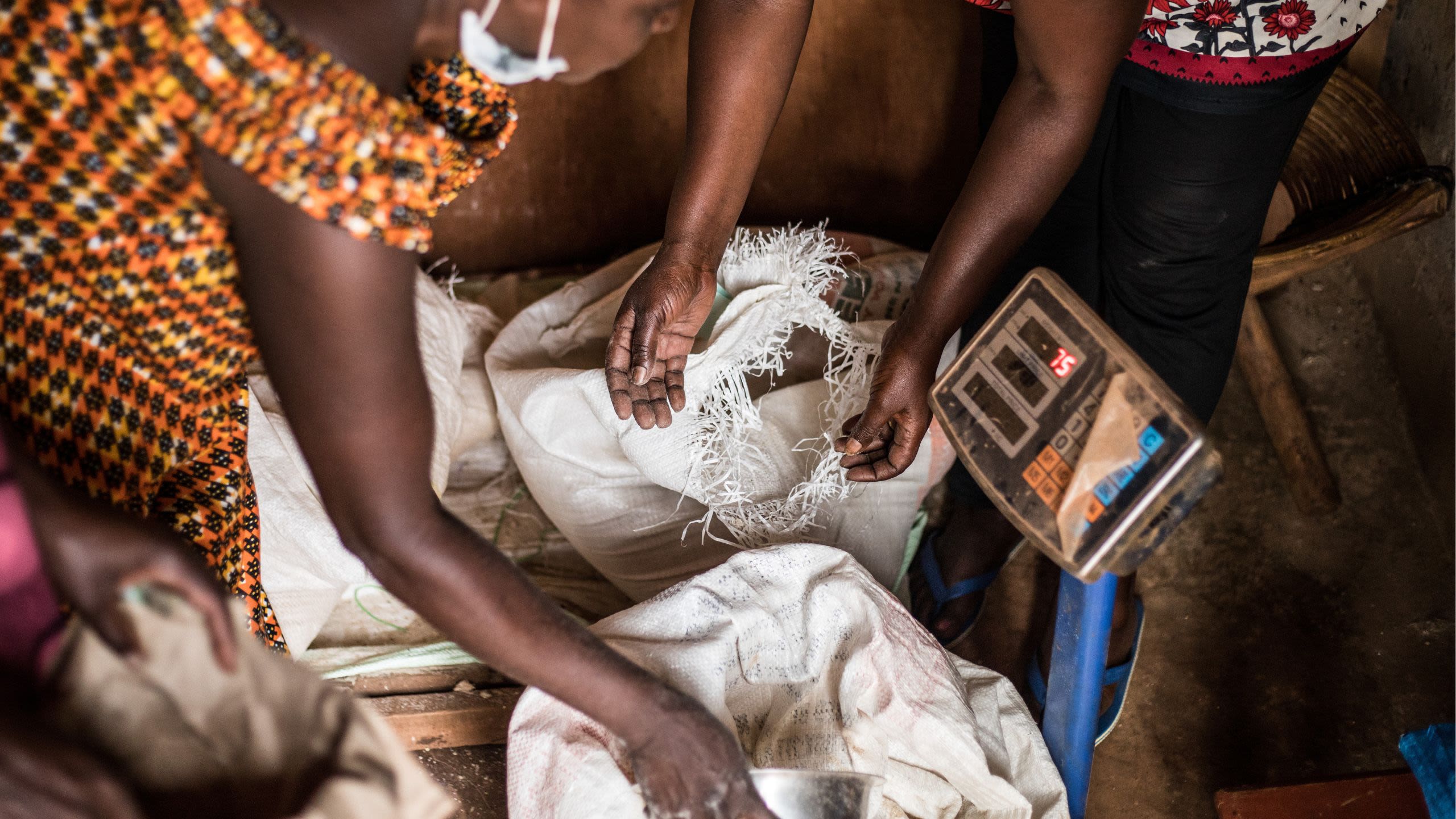 Focused view on the hands of women from the Urumuri group as they weigh and package poultry feed.