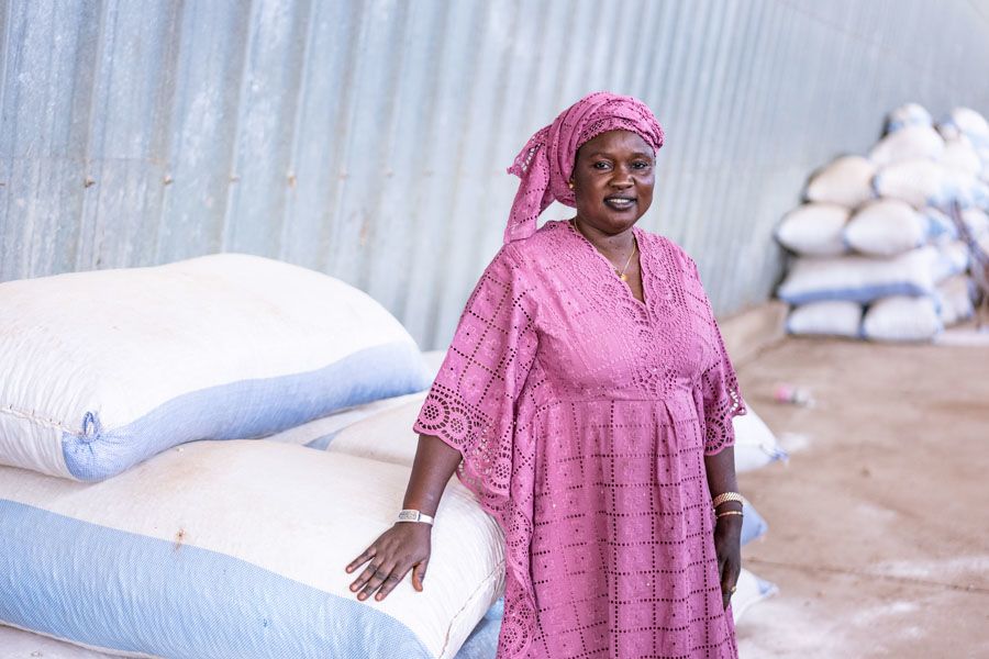 A woman smiling in front of a pile of large seeds bags.